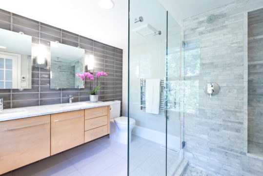 A contemporary modern bathroom design. Glass enclosed shower stall with marble tiles, vanity and double sink counter. A newly remodeled bathroom.